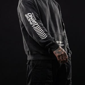 May include: Dark gray hoodie with the text "UNDER GRND culture" printed in white on the left sleeve. The hoodie has a drawstring hood and a kangaroo pocket. The model is wearing black cargo pants.