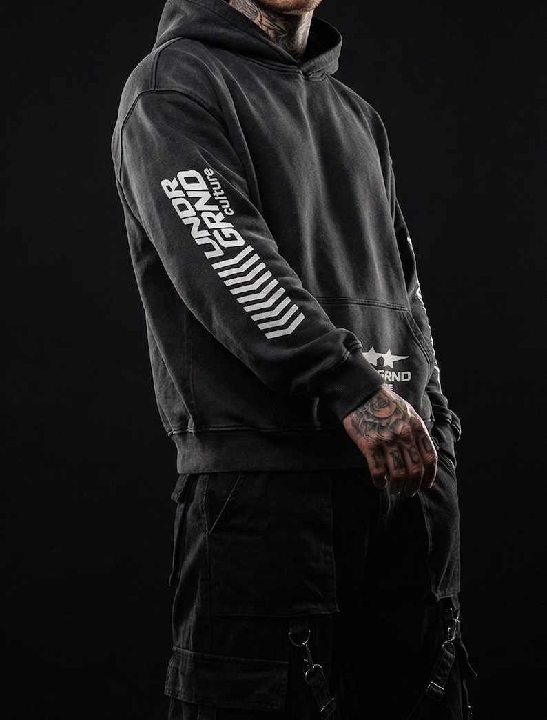 May include: Dark gray hoodie with the text "UNDER GRND culture" printed in white on the left sleeve. The hoodie has a drawstring hood and a kangaroo pocket. The model is wearing black cargo pants.