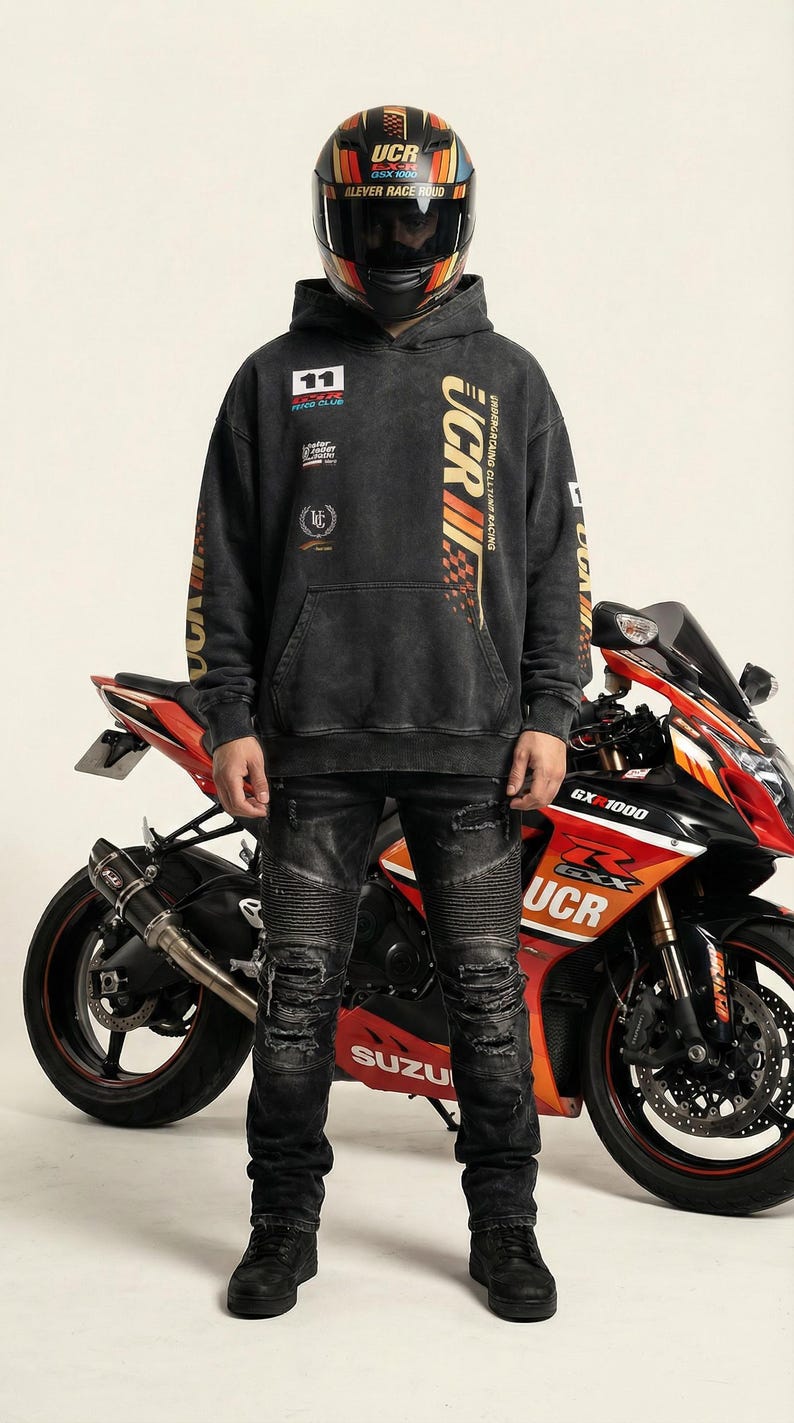 May include: A person wearing a black hoodie with "UCR" and racing graphics, distressed black jeans, and a motorcycle helmet. A red and black Suzuki GSX-1000 motorcycle is behind the person.