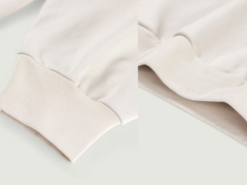 May include: Close-up of a cream-colored sweatshirt sleeve and cuff. The cuff is ribbed and the sleeve is made of a soft, smooth fabric. The background is a solid, light color.