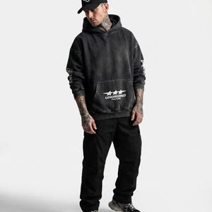 May include: A person wearing a black hoodie with the text "UNDRGRND CULTURE" and a black baseball cap with a white "UC" logo. The person is also wearing black cargo pants and black and gray sneakers.