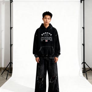 May include: A black acid-wash hooded sweatshirt featuring a white graphic print that reads Tsukiji Outer Market, Tokyo, Japan, with a fish illustration and a small Japanese flag. The hoodie is paired with matching black distressed wide-leg denim jeans.