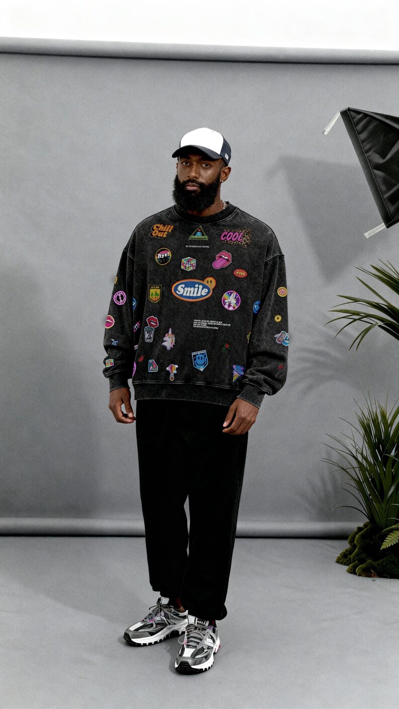 Pu&ograve; includere: Una felpa nera con diverse toppe colorate e le parole "Chill Out", "Cool" e "Smile". La persona indossa anche pantaloni neri, un berretto da baseball bianco e nero e scarpe da ginnastica grigie e bianche.