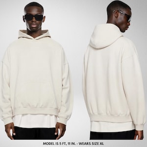 May include: A cream-colored hoodie with a front pocket and a hood. The model is wearing sunglasses and black pants. The hoodie is oversized and has a relaxed fit. The model is 5 ft, 11 in. and wears size XL.