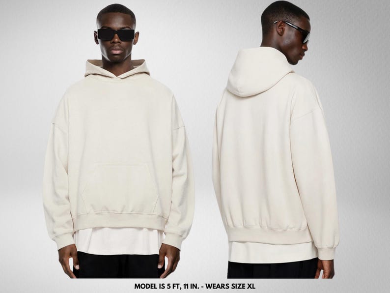 May include: A cream-colored hoodie with a front pocket and a hood. The model is wearing sunglasses and black pants. The hoodie is oversized and has a relaxed fit. The model is 5 ft, 11 in. and wears size XL.