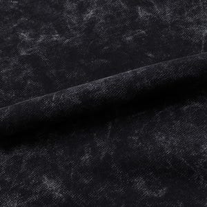May include: Close-up of a black fabric with a textured, distressed appearance. The fabric has a mottled pattern with lighter gray areas, creating a worn or vintage aesthetic. The material is folded, showing the texture and drape of the fabric.