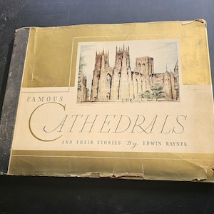 Op de afbeelding: Een vintage boek getiteld "Famous Cathedrals and Their Stories" door Edwin Rayner. De omslag toont een aquarel illustratie van een kathedraal met beige en gouden accenten. De kaft van het boek is licht versleten.