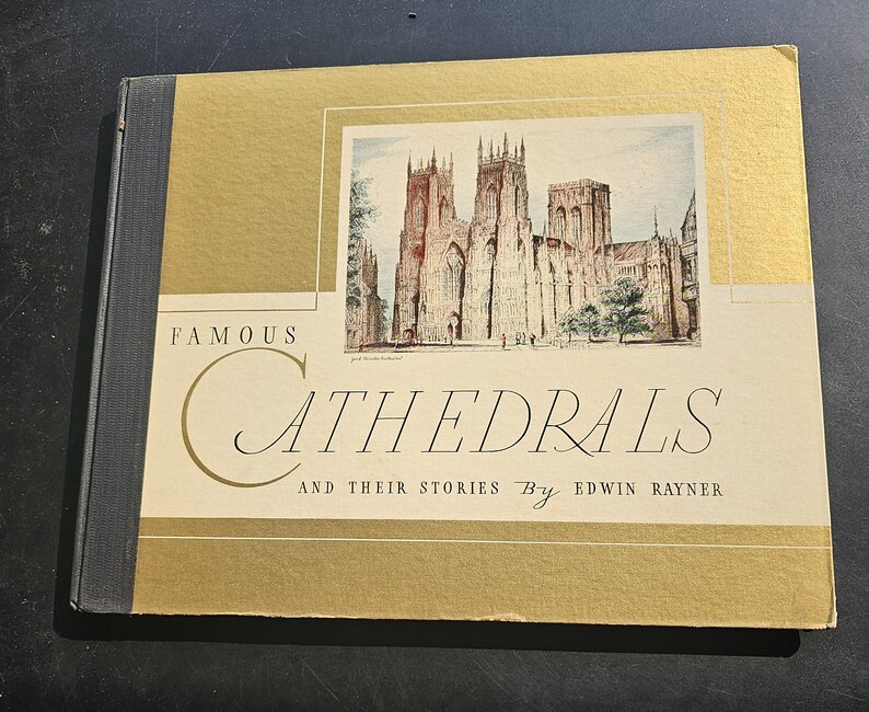 Op de afbeelding: Een vintage boek getiteld "Famous Cathedrals and Their Stories" door Edwin Rayner. De omslag is goud en cr&egrave;me, met een illustratie van een kathedraal. De rug van het boek is donkergrijs.