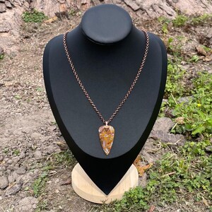 Op de afbeelding: Een koperen ketting met een grote, traanvormige hanger gemaakt van bruin, geel en wit agaat.
