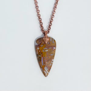 Op de afbeelding: Een koperen ketting met een hanger van bruin en wit agaat. De hanger heeft de vorm van een traan en heeft een koperen accent in de vorm van een diamant aan de bovenkant.