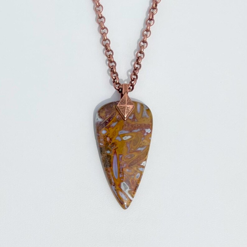 Op de afbeelding: Een koperen ketting met een hanger van bruin en wit agaat. De hanger heeft de vorm van een traan en heeft een koperen accent in de vorm van een diamant aan de bovenkant.