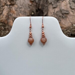 May include: A pair of copper dangle earrings with a round sunstone bead on each earring.
