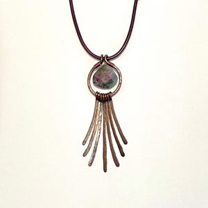 May include: A copper necklace with a green and pink gemstone pendant and a fringe of copper strands.