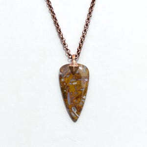 Op de afbeelding: Een koperen ketting met een hanger van bruin en wit agaat. De hanger heeft de vorm van een traan en heeft een koperen accent aan de bovenkant.