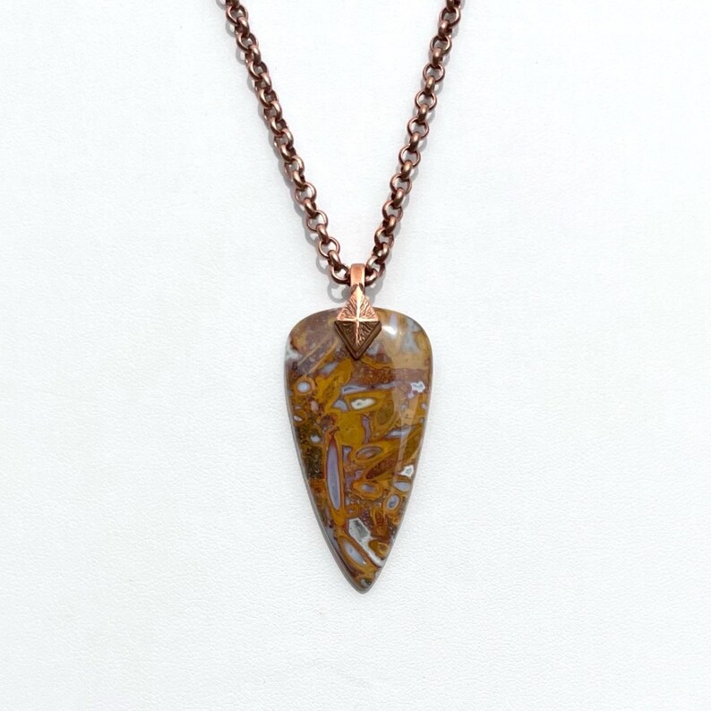 Op de afbeelding: Een koperen ketting met een hanger van bruin en wit agaat. De hanger heeft de vorm van een traan en heeft een koperen accent aan de bovenkant.