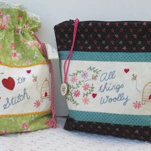 Może przedstawiać: Dwie torby materiałowe z haftowanymi wzorami. Zielona torba ma serce z napisem "to stitch" i ul. Czarno-niebieska torba ma ul i napis "All things woolly".