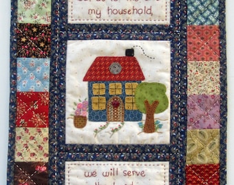 May include: A quilted wall hanging with a patchwork design featuring a house, a tree, and hearts. The text reads "But as for me and my household, we will serve the Lord." Jos 24:15