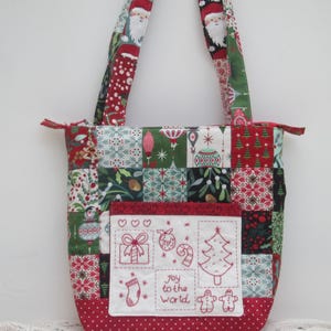 Pode incluir: Uma bolsa de mão de patchwork vermelha e verde com um bolso branco com desenhos de Natal bordados. O bolso tem o texto "Joy to the World" e imagens de uma árvore de Natal, uma meia, um homem de gengibre, um bastão de caramelo, um presente e um enfeite.
