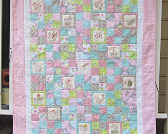 Puede incluir: Una colcha rosa y blanca con un diseño de patchwork. Cada cuadrado presenta un patrón de tela diferente y palabras bordadas, incluyendo "acceptance", "give", "home", "shelter", "dream", "fun", "wings", "brother", "joy", y "smiles".