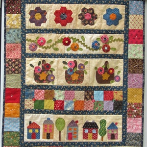 May include: A colorful quilt with a patchwork design featuring hearts, flowers, houses, and baskets. The quilt is made with a variety of fabrics in shades of red, blue, green, yellow, and brown.