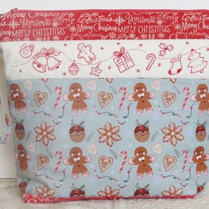 May include: A blue and white fabric zippered pouch with a Christmas theme. The pouch has a red zipper and a red and white fabric strap. The front of the pouch features a repeating pattern of gingerbread men, candy canes, snowflakes, and Christmas pudding.