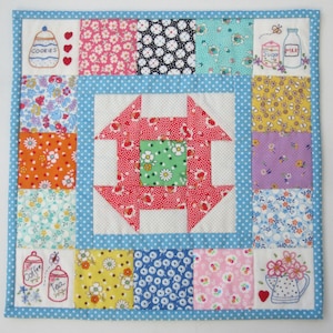 May include: A patchwork quilt with a red and white center and a blue border. The quilt is made up of squares of different fabrics with floral patterns. The quilt is decorated with embroidered images of jars, flowers, and other kitchen items.