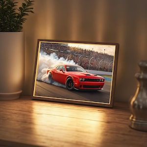 May include: A red Dodge Challenger muscle car with black accents, drifting on a race track, leaving a trail of smoke behind it. The car is framed in a wooden picture frame.