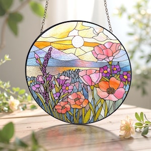 May include: Round stained glass panel featuring a vibrant floral landscape. The design includes pink and orange poppies, purple flowers, and a sunset with a white sun. The panel is framed in black and hangs from a chain.