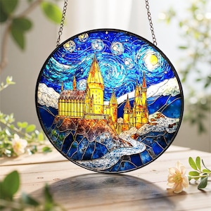 Könnte beinhalten: Rundes Buntglasfenster mit einem Schloss unter einem Sternenhimmel. Das Kunstwerk hat einen schwarzen Metallrahmen und wird von einer Kette gehalten. Das Schloss ist gelb und orange, mit einem blauen Fluss und Himmel.