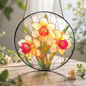 May include: A round stained glass window featuring a bouquet of daffodils. The flowers have yellow petals with orange and pink centers, and green stems and leaves. The window is framed in black and hangs from a chain.