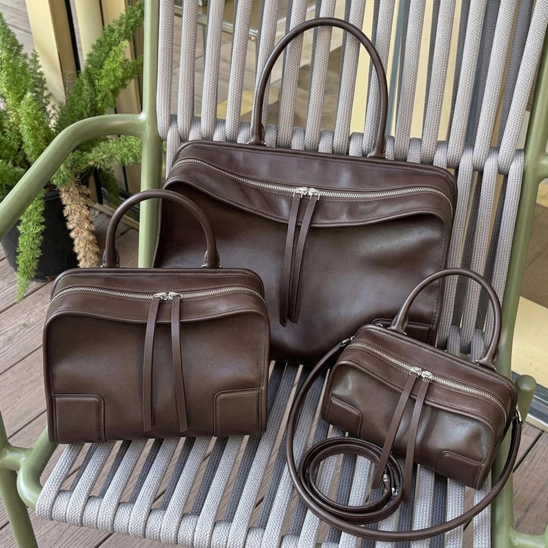 May include: Three brown leather handbags of varying sizes. The largest has a top handle, the medium has a top handle, and the smallest has a shoulder strap. All have silver zippers and matching leather zipper pulls.