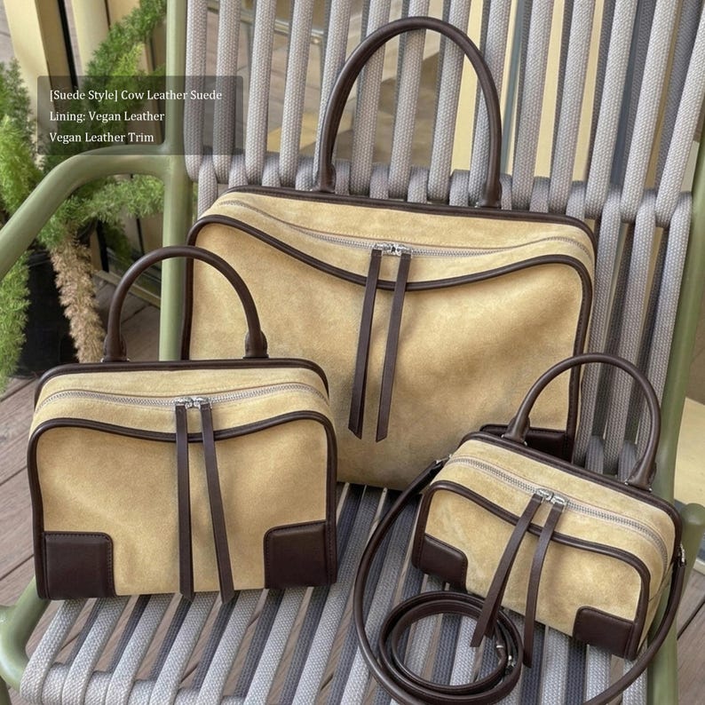 May include: Three tan suede-style handbags with brown leather trim and handles. The bags vary in size, with a large tote, a medium satchel, and a small crossbody bag. Each bag has a zipper closure and a minimalist design.