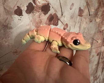 May include: A small, multi-colored, segmented toy lizard with a pink, yellow, and green color scheme. The toy has a textured surface and large, black eyes.