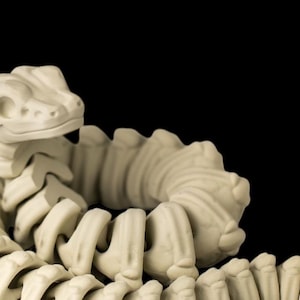 Peut inclure: Un jouet squelette de dinosaure articulé de couleur crème, avec une tête détaillée et un corps segmenté. Le jouet est présenté enroulé sur un fond noir, mettant en valeur sa structure squelettique.