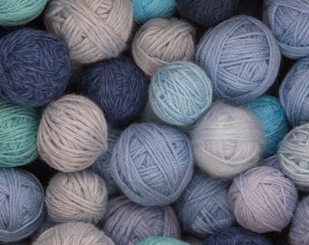 May include: A collection of yarn balls in various shades of blue, from light sky blue to deep navy. The balls are tightly wound and arranged closely together, creating a textured, colorful display. Ideal for knitting and crochet projects.