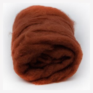 May include: A dense, cylindrical roll of raw, unspun wool fiber in a deep, earthy terracotta orange color. The texture is soft, fibrous, and voluminous, showing the natural, matted appearance of processed sheep wool ready for spinning or felting.