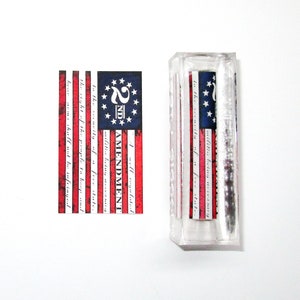 May include: A rectangular, clear acrylic block with a printed design of the American flag and the text "2ND AMENDMENT". The flag design features red and white stripes, a blue field with white stars, and the text of the Second Amendment.