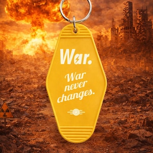Könnte beinhalten: Gelber Schlüsselanhänger im Motel-Stil mit dem weißen Schriftzug "War. War never changes.". Der Hintergrund zeigt eine Atombombenexplosion und eine zerstörte Stadt. Der Schlüsselanhänger hat einen Metallring.