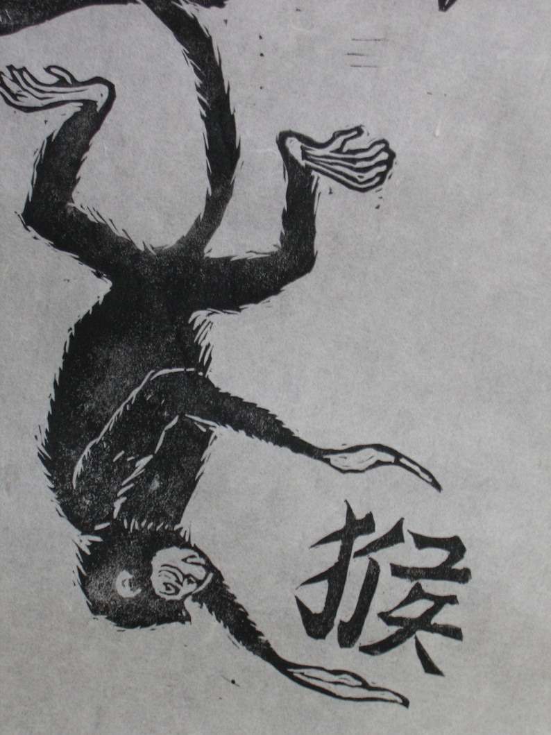 May include: Black and white woodcut print of a monkey hanging upside down with the Chinese character for "monkey" printed below.