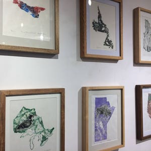 K&ouml;nnte beinhalten: Eine Wandmontage von gerahmten Kunstwerken mit verschiedenen Karten kanadischer Provinzen. Die Karten sind in verschiedenen Farben und Stilen gedruckt, darunter eine Karte von Ontario mit einem Seetaucher, eine Karte von Manitoba mit einem Bison und eine Karte von Prince Edward Island mit einem Blumendesign.