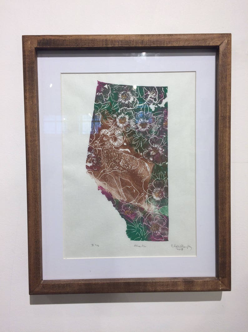 K&ouml;nnte beinhalten: Ein gerahmter Druck einer gr&uuml;nen, rosa und braunen Landschaft mit einer Silhouette eines Dickhornschafs. Der Druck ist mit "Alberta" betitelt und von "Elizabeth Willoughby 2019" signiert.