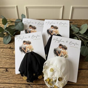 Puede incluir: Recuerdos de boda con una imagen impresa de una pareja, los nombres "Mazlum & Berfin" y la fecha "14.06.2025". Algunos recuerdos están adornados con tela blanca y negra y monedas de oro.