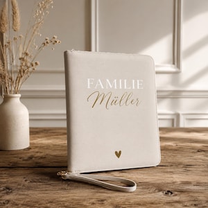 Könnte beinhalten: Eine beigefarbene, rechteckige Dokumentenmappe mit Reißverschluss und Handschlaufe. Auf der Vorderseite steht der weiße Schriftzug FAMILIE und der goldene Schreibschrift-Text Müller, mit einem kleinen goldenen Herzsymbol darunter.