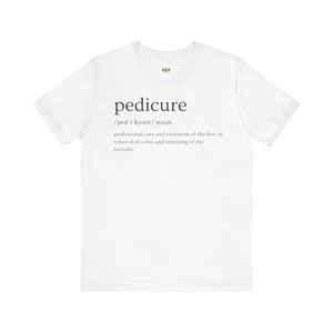 May include: White t-shirt with the word "pedicure" and its definition printed in black text.