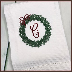May include: White kitchen towel with an embroidered Christmas wreath with a red bow and the letter C in the center.