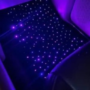 Puede incluir: El techo interior de un coche est&aacute; iluminado con numerosas luces peque&ntilde;as, brillantes, moradas y blancas, creando un efecto de noche estrellada. Las luces est&aacute;n dispersas por la superficie azul oscuro, con algunas luces moradas en los laterales.