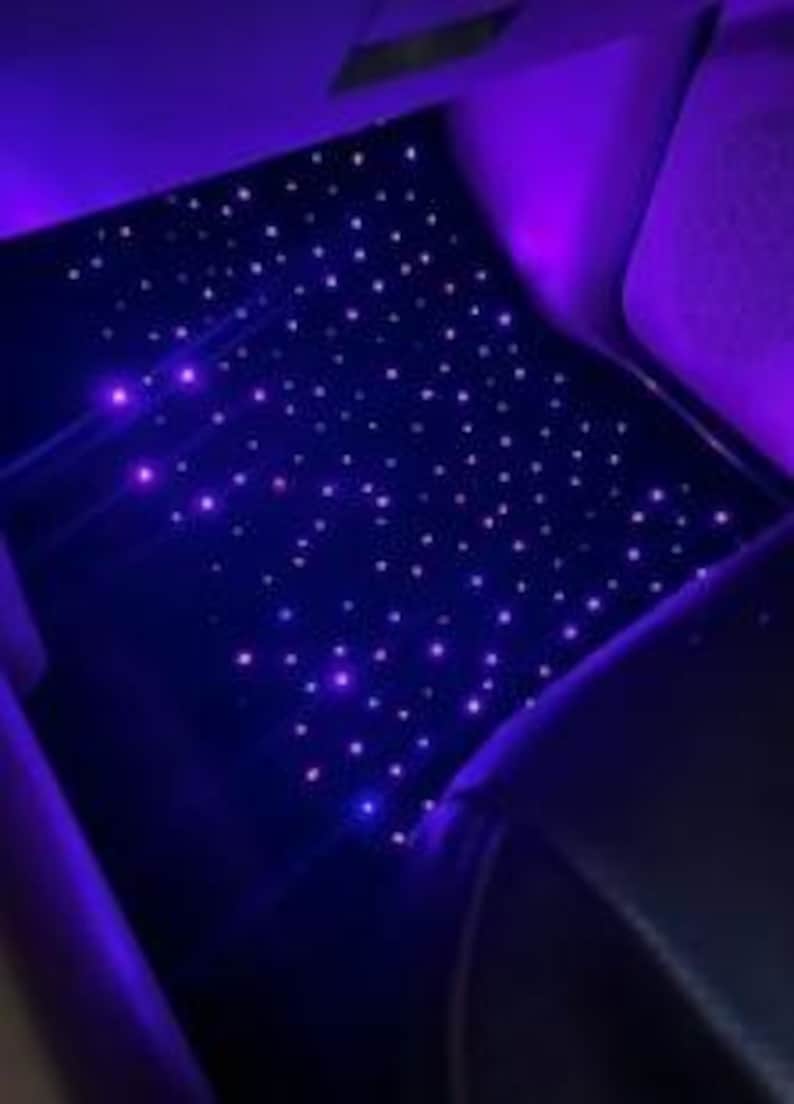 Puede incluir: El techo interior de un coche est&aacute; iluminado con numerosas luces peque&ntilde;as, brillantes, moradas y blancas, creando un efecto de noche estrellada. Las luces est&aacute;n dispersas por la superficie azul oscuro, con algunas luces moradas en los laterales.