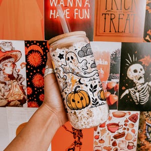 May include: A clear glass tumbler with a bamboo lid and straw, decorated with Halloween-themed illustrations. The design includes a ghost, pumpkin, stars, and other festive elements. The background features Halloween-themed posters. The text "GIRLS JUST WANNA HAVE FUN" is visible.