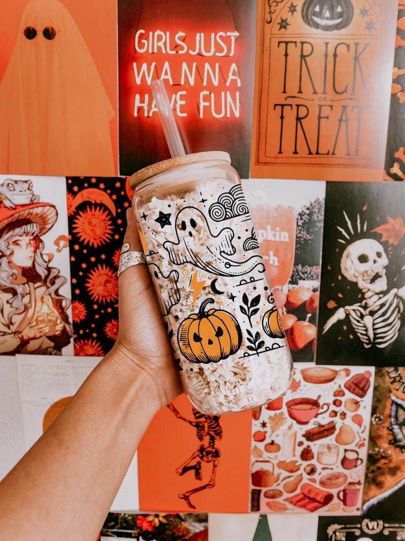 May include: A clear glass tumbler with a bamboo lid and straw, decorated with Halloween-themed illustrations. The design includes a ghost, pumpkin, stars, and other festive elements. The background features Halloween-themed posters. The text "GIRLS JUST WANNA HAVE FUN" is visible.