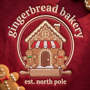 May include: A dark red fabric featuring an embroidered circular logo with the text gingerbread bakery and est. north pole. The design shows a gingerbread house with a red and white striped awning, two gingerbread cookies, and a rolling pin.
